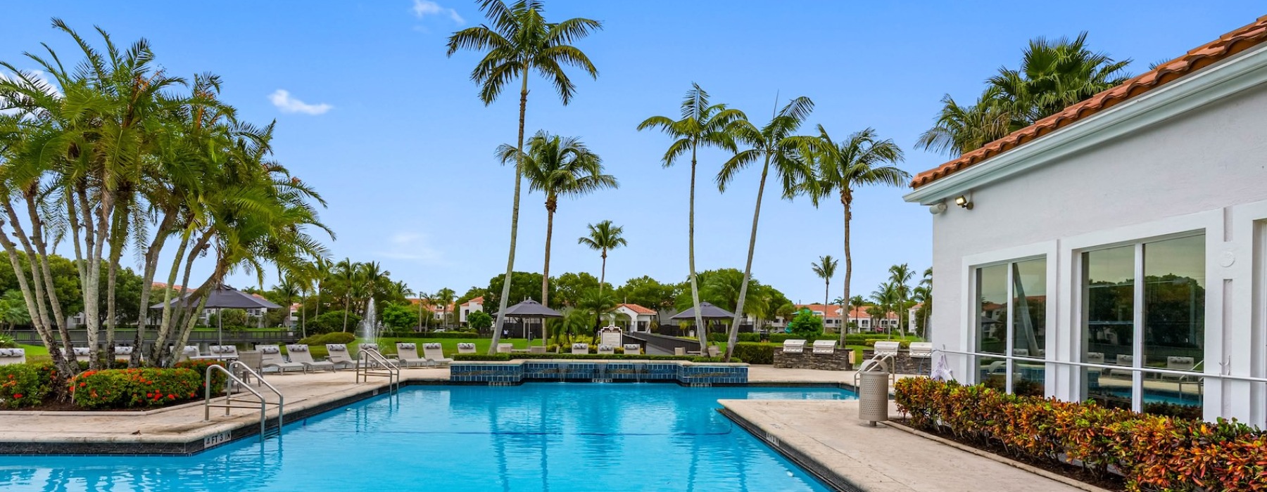 Resort-style swimming pool at The Palms of Doral, Doral, FL, featuring a large sundeck, palm trees, and poolside cabanas for resident relaxation.