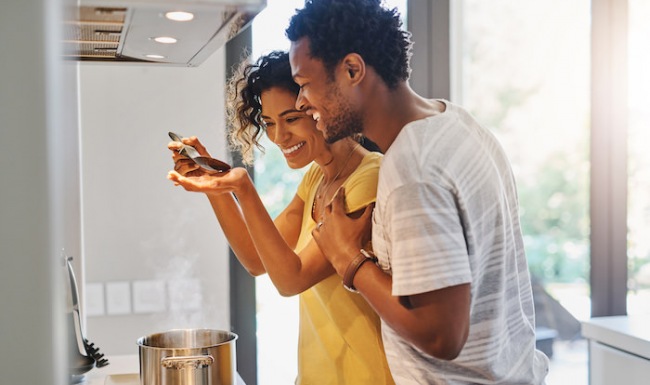 Lifestyle Happy couple smiling while cooking on a gas stove in a modern apartment kitchen, demonstrating the lifestyle at The Palms of Doral.