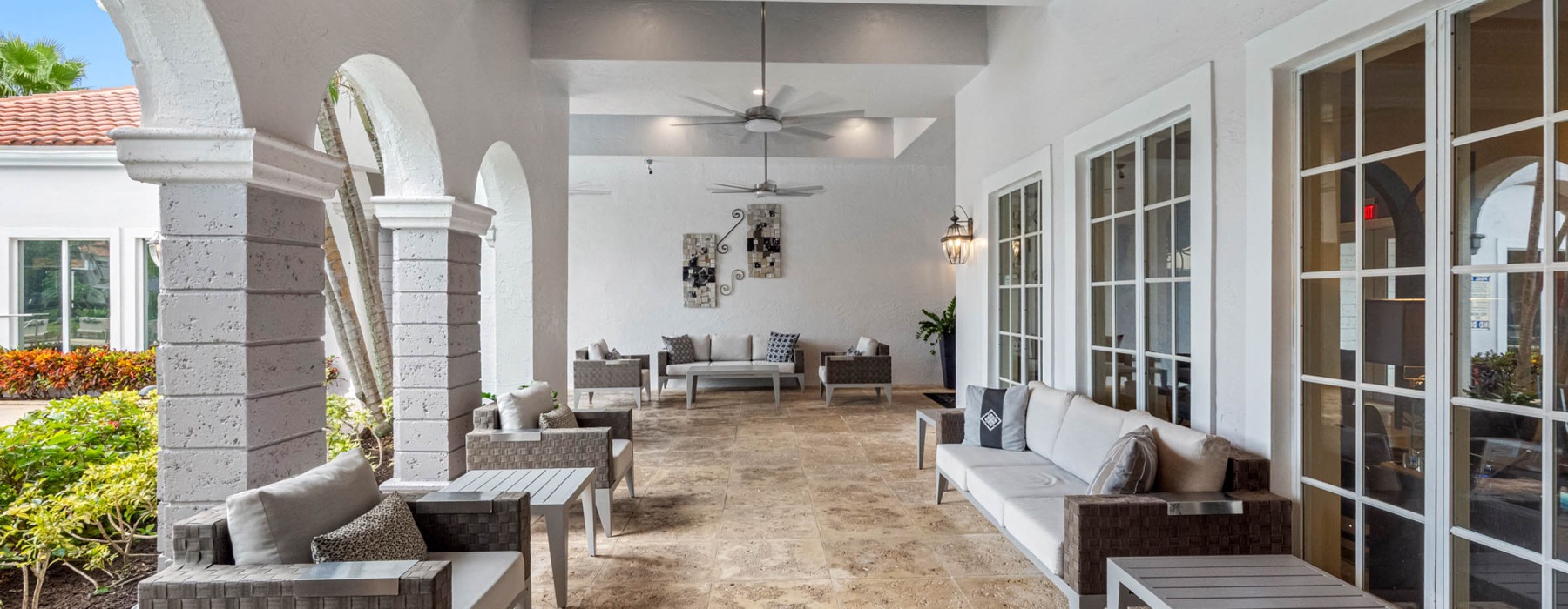 Covered outdoor resident lounge with ceiling fans, modern furniture, and archways outside the clubhouse at The Palms of Doral, FL.