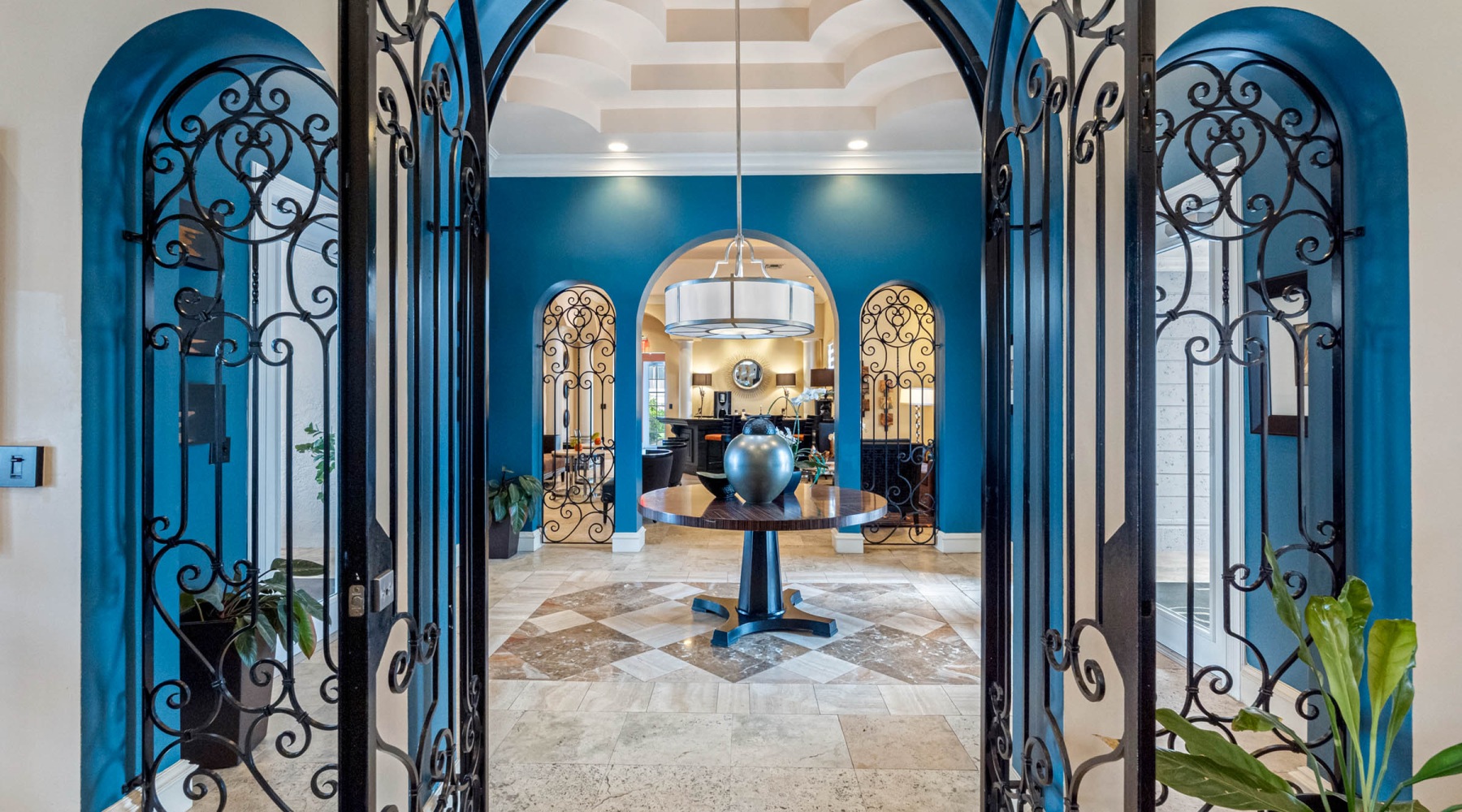 Beautiful Entry Lobby Ornate black iron entry gates opening into the luxury clubhouse foyer with bold teal walls and vaulted ceiling at The Palms of Doral.
